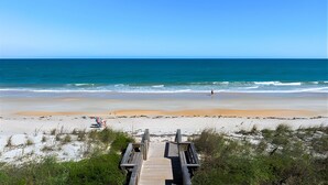 A wooden boardwalk leading to a beach with a clear view of the ocean.