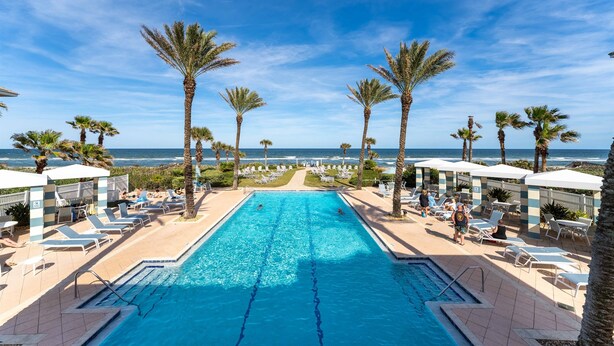 A swimming pool with lounge chairs and palm trees, overlooking the ocean.