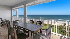 A covered outdoor area with a table and chairs, overlooking a beach.