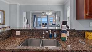 A kitchen with granite countertops, a double sink, and a view to the living area.