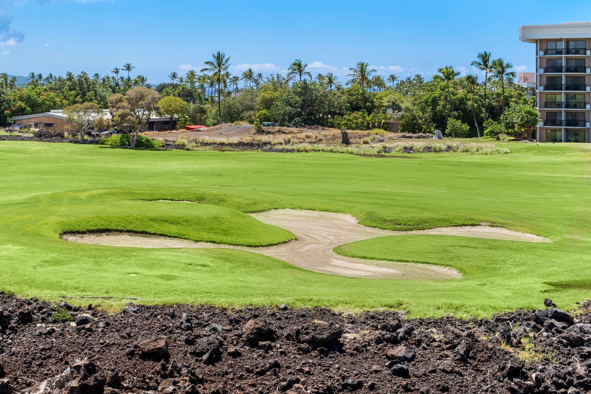 Un campo da golf con bunker, palme e un edificio sullo sfondo.