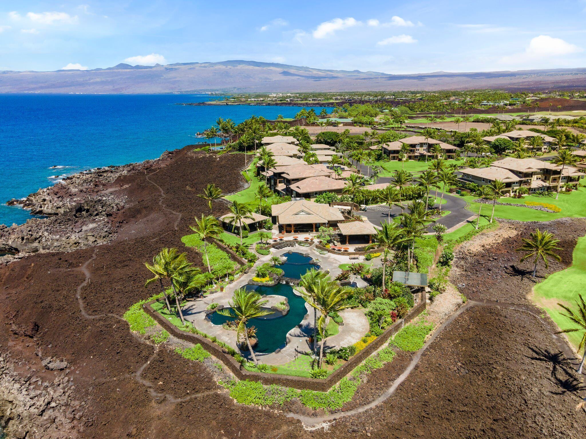An aerial view of a resort with multiple buildings, a central pool, and a coastline.