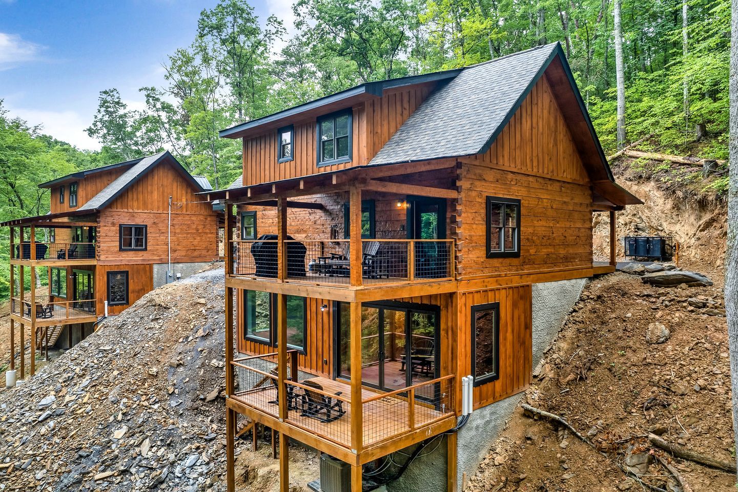 A wooden cabin with a balcony and a deck, surrounded by a forest.