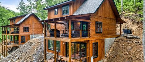 A wooden cabin with a balcony and a deck, surrounded by a forest.