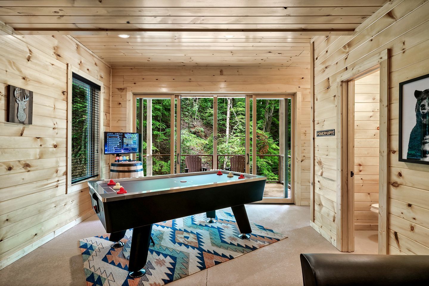 Interior em madeira com mesa de bilhar, televisão e vista para a floresta.