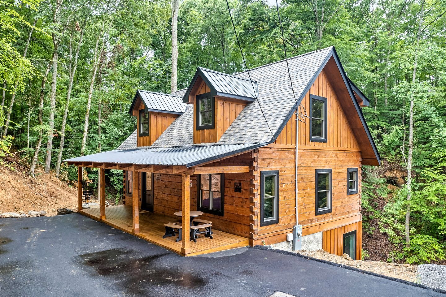 A two-story wooden cabin with a covered porch and a small outdoor seating area.