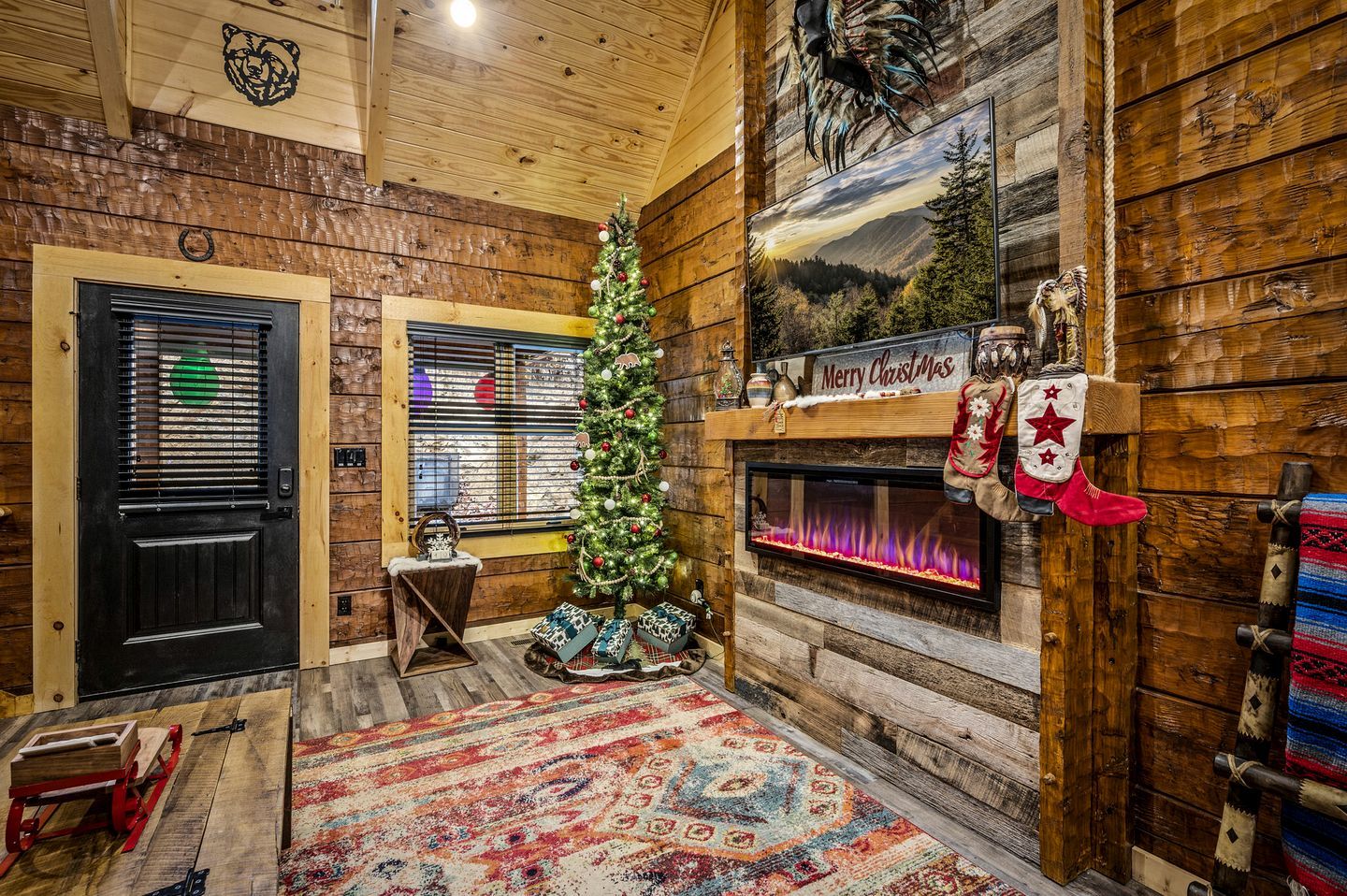 A cozy log cabin interior with a fireplace, a Christmas tree, and rustic decor.