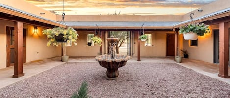 A courtyard with a central fountain, potted plants, and hanging planters.