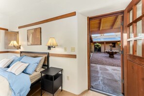 A bedroom with a bed, bedside tables, wall-mounted lamps, and a view of an outdoor courtyard with a fountain.