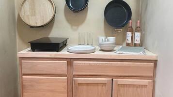 Cocina compacta con encimera de madera, tres ollas colgantes, un lavamanos pequeño y una botella de vino.