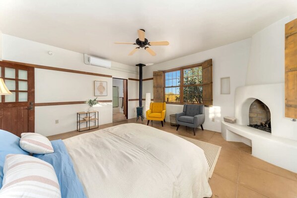 A bedroom with a bed, a fireplace, a ceiling fan, and a window with a view.