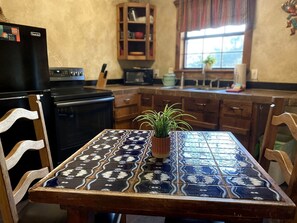 Una cocina con una mesa de baldosas, sillas de madera, un refrigerador, un microondas y un armario.