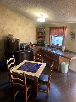 Una cocina compacta con una mesa de comedor, sillas de madera, un refrigerador, un microondas y un armario.