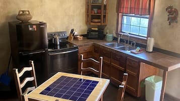 A compact kitchen with a dining table, wooden chairs, a refrigerator, a microwave, and a cabinet.