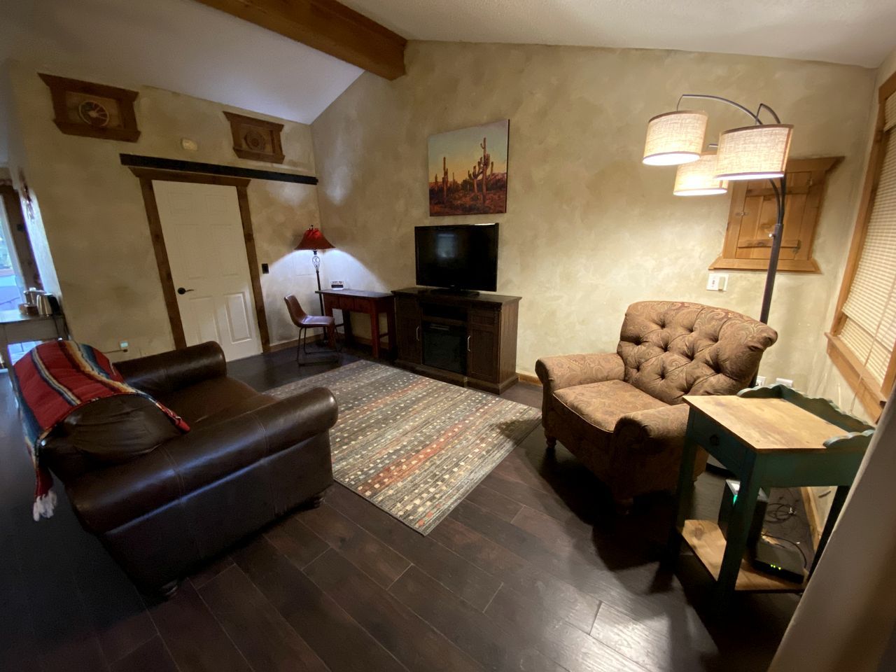 Ein Wohnzimmer mit einem braunen Ledersofa, einem gepolsterten Sessel, einem Holztisch, einem Flachbildfernseher und einem gemusterten Teppich.