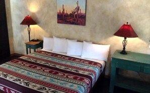Una cama con una colcha estampada, dos mesitas de noche con lámparas, y un cuadro colgado en la pared.