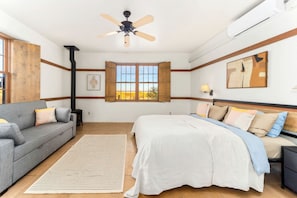 Un dormitorio con cama, sofá, ventana con vistas, ventilador de techo y aire acondicionado.