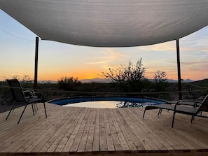 Une terrasse en bois avec une piscine, des chaises longues et une vue sur le coucher de soleil.