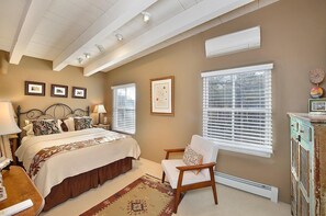 Ein Schlafzimmer mit Bett, Sessel, Kommode und einem Fenster mit Jalousien.