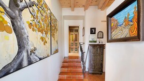 Un pasillo con una escalera, un cuadro de un árbol grande y una obra enmarcada en la pared.