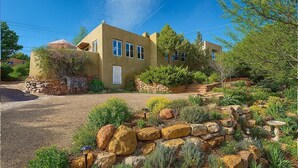 Una casa de dos pisos con fachada de piedra, un porche delantero y un jardín ajardinado con rocas y arbustos.