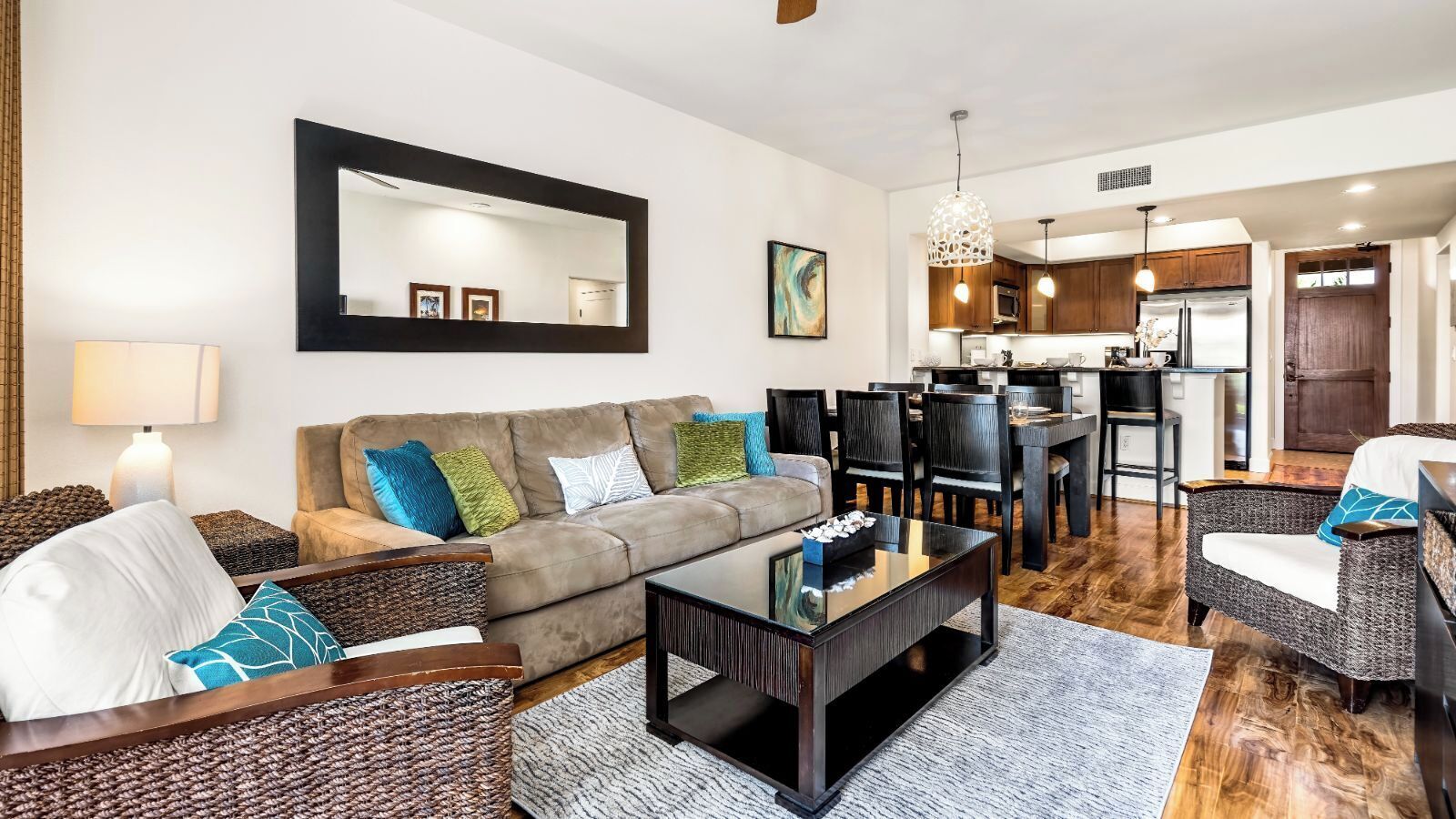 Ein modernes Wohnzimmer mit einer Couch, einem Couchtisch und Korbstühlen. Es gibt eine Essecke mit Tisch und Stühlen, und im Hintergrund eine Küche.