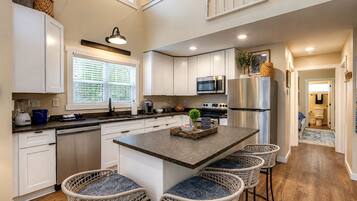 A modern kitchen with white cabinetry, a central island with bar stools, a built-in microwave, and a stainless steel refrigerator.