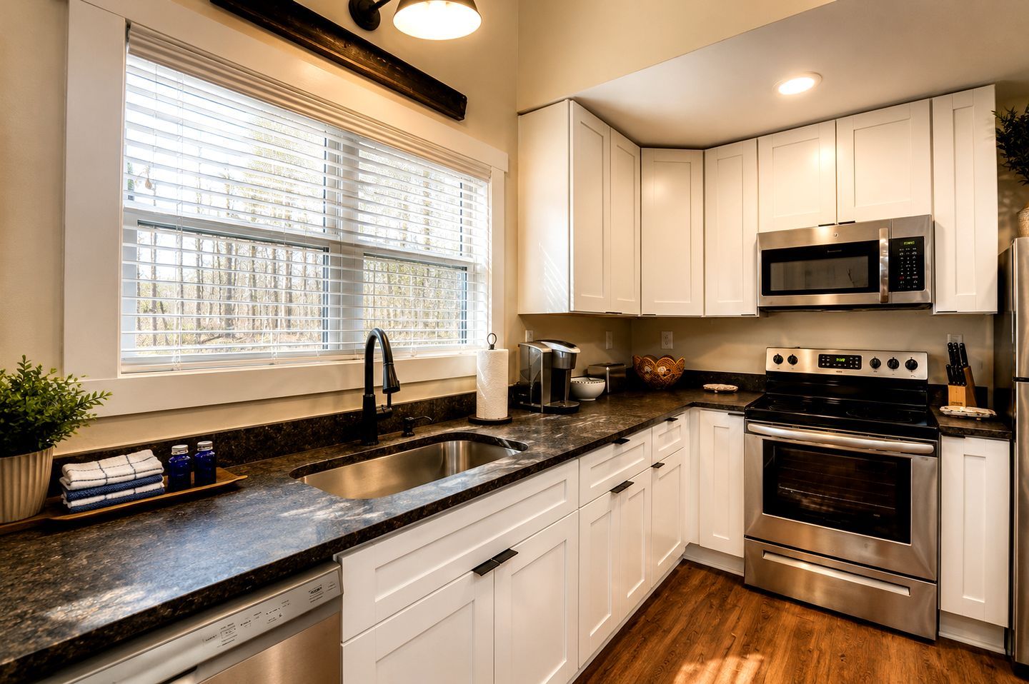 A modern kitchen with white cabinets, a stainless steel sink, a built-in microwave, and an oven.
