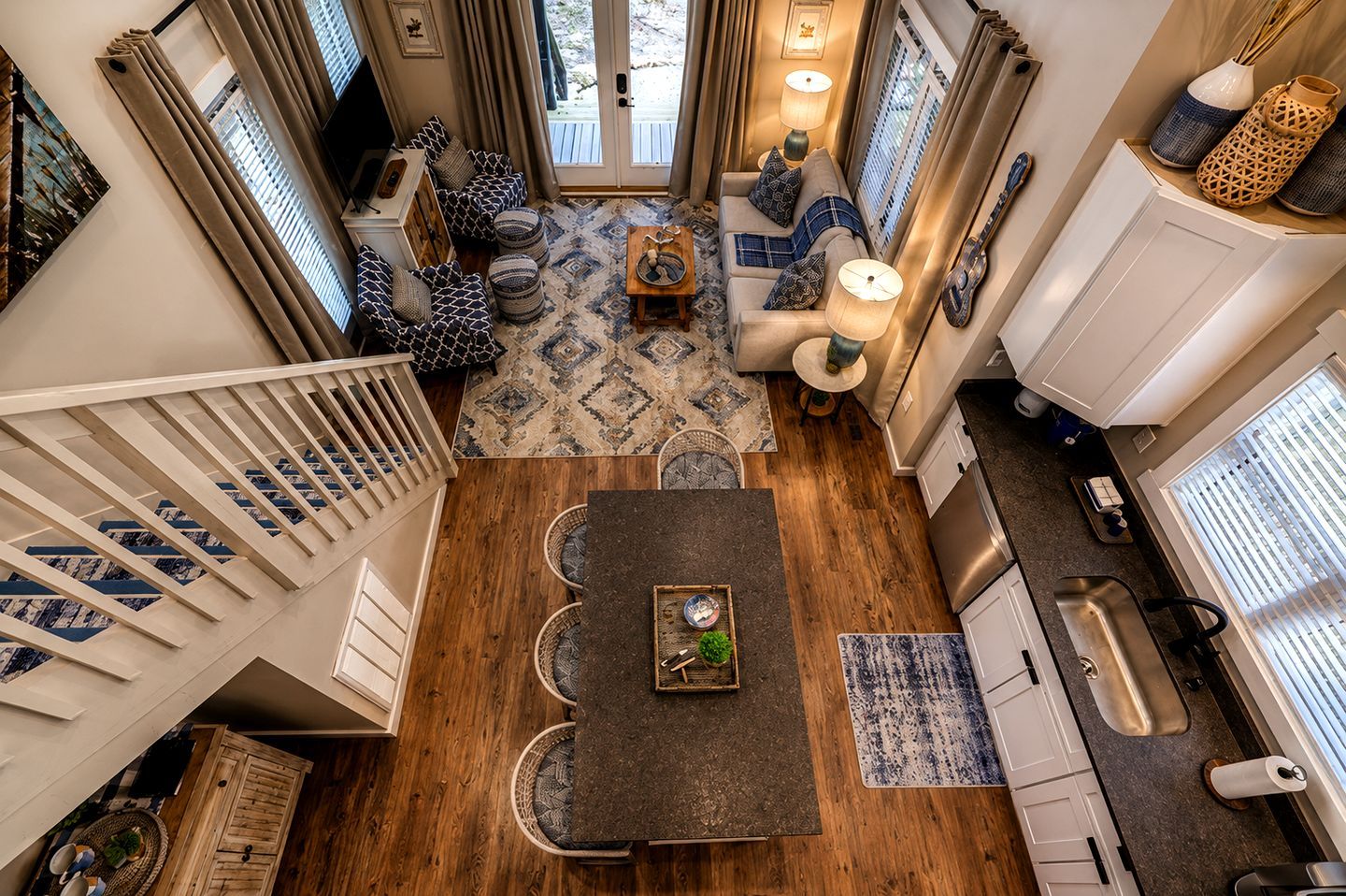 A spacious living area with a wooden floor, a sofa set, a dining table, and a kitchen area with a sink and cabinets.