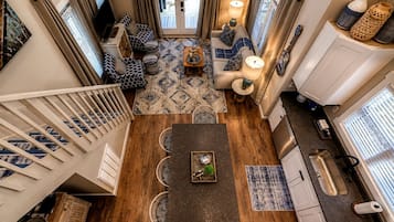 A spacious living area with a wooden floor, a sofa set, a dining table, and a kitchen area with a sink and cabinets.