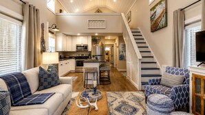 A spacious living area with a sofa, coffee table, and a staircase leading to a kitchen area. - Embrace Nature in this Cozy Cabin with Fire Pit in Monteagle, Tennessee (Monteagle)