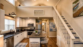 A spacious kitchen with a central island, stainless steel appliances, and a wooden staircase.