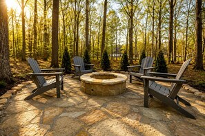 A stone fire pit surrounded by Adirondack chairs in a forest setting. - Embrace Nature in this Cozy Cabin with Fire Pit in Monteagle, Tennessee (Monteagle)