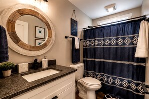 Ein Badezimmer mit rundem Spiegel, Waschbecken, Toilette und Duschvorhang.