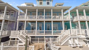 Une maison à plusieurs étages située en bord de mer, dotée de balcons, d’une terrasse en bois et d’un espace salon extérieur.