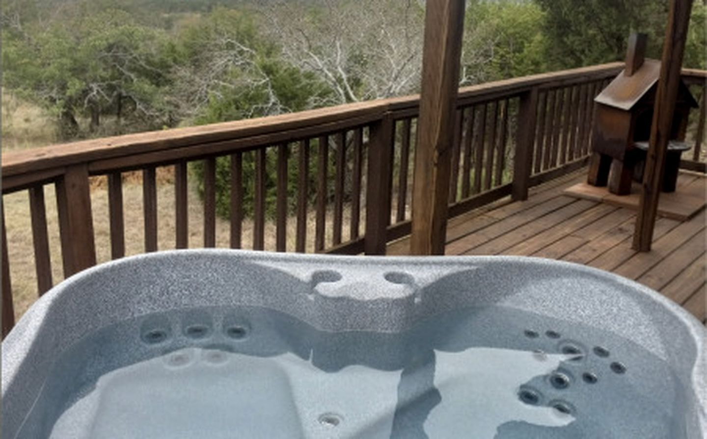 Un jacuzzi en una terraza de madera con vista a árboles.