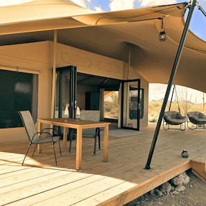 An outdoor wooden deck with a table and chairs, a hanging chair, and a covered area with a view of the landscape.