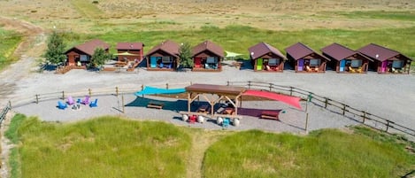 A campground with multiple cabins, a covered seating area, and a dirt path.
