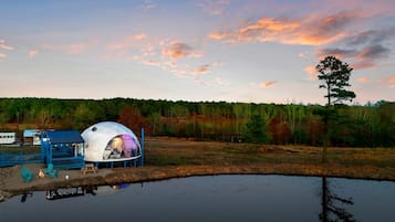 A dome-shaped tent with a blue exterior and a white interior, situated next to a body of water with a reflection.