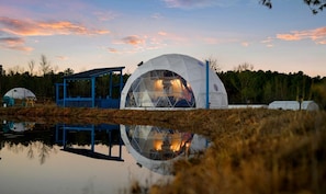 A dome-shaped structure with a glass ceiling, surrounded by a blue pavilion, and reflecting in a body of water.