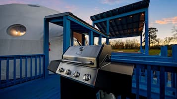 Uma área de churrasco coberta ao ar livre, com estrutura azul, uma tenda e um deck de madeira.
