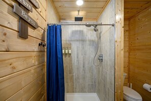 A wooden cabin bathroom with a shower, toilet, and a sign on the wall. - Incredi-Dome Family Experience in Broken Bow, OK (Broken Bow)