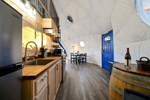 A compact kitchen with wooden cabinets, a sink, and a dining area with a table and chairs. - Incredi-Dome Family Experience in Broken Bow, OK (Broken Bow)