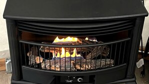 A black wood-burning stove with a fire burning inside, a control panel, and a metal grate. - Geodome on Creek, Great Getaway, WIFI & Hot Shower near Boone, NC (Purlear)