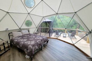 A geodesic dome tent with a bed, a small table, and a chair.