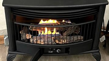 A black wood-burning stove with a fire burning inside, a control panel, and a metal grate.