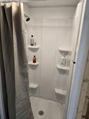 A shower with a beige curtain, a handheld showerhead, and shelves with toiletries.