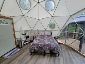 A room with a bed, a shelf with items, a door, and a window.