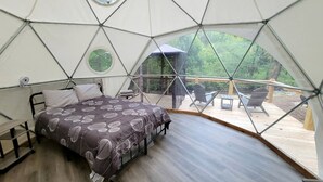 Una tienda en forma de domo geodésico con una cama, una mesita y una silla.