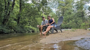 Dos personas sentadas en una silla junto a un río en una zona boscosa.